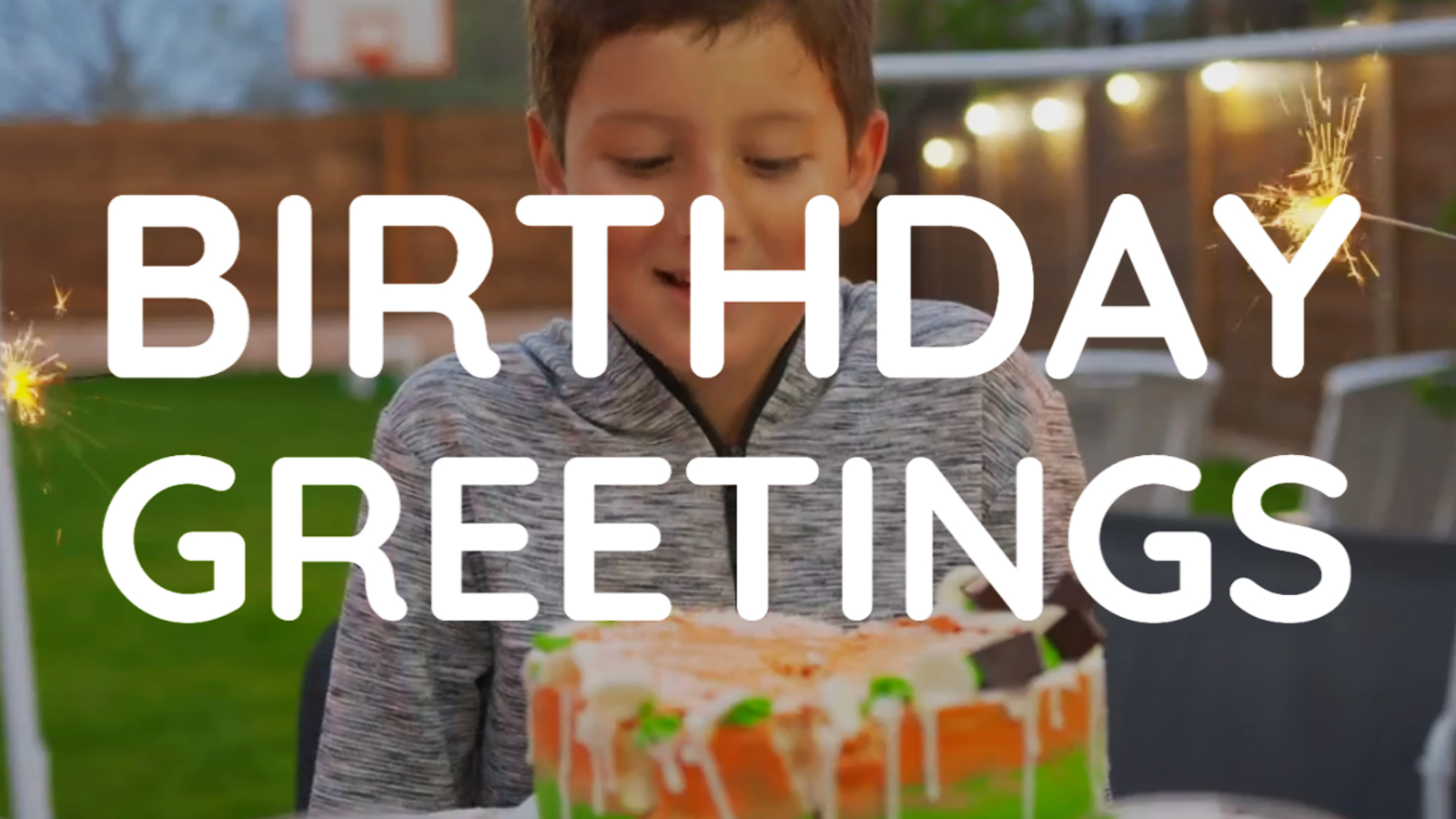 A young boy smiling with a sparkler-lit birthday cake, with the words "birthday greetings" displayed across the image, created using Biteable video maker.