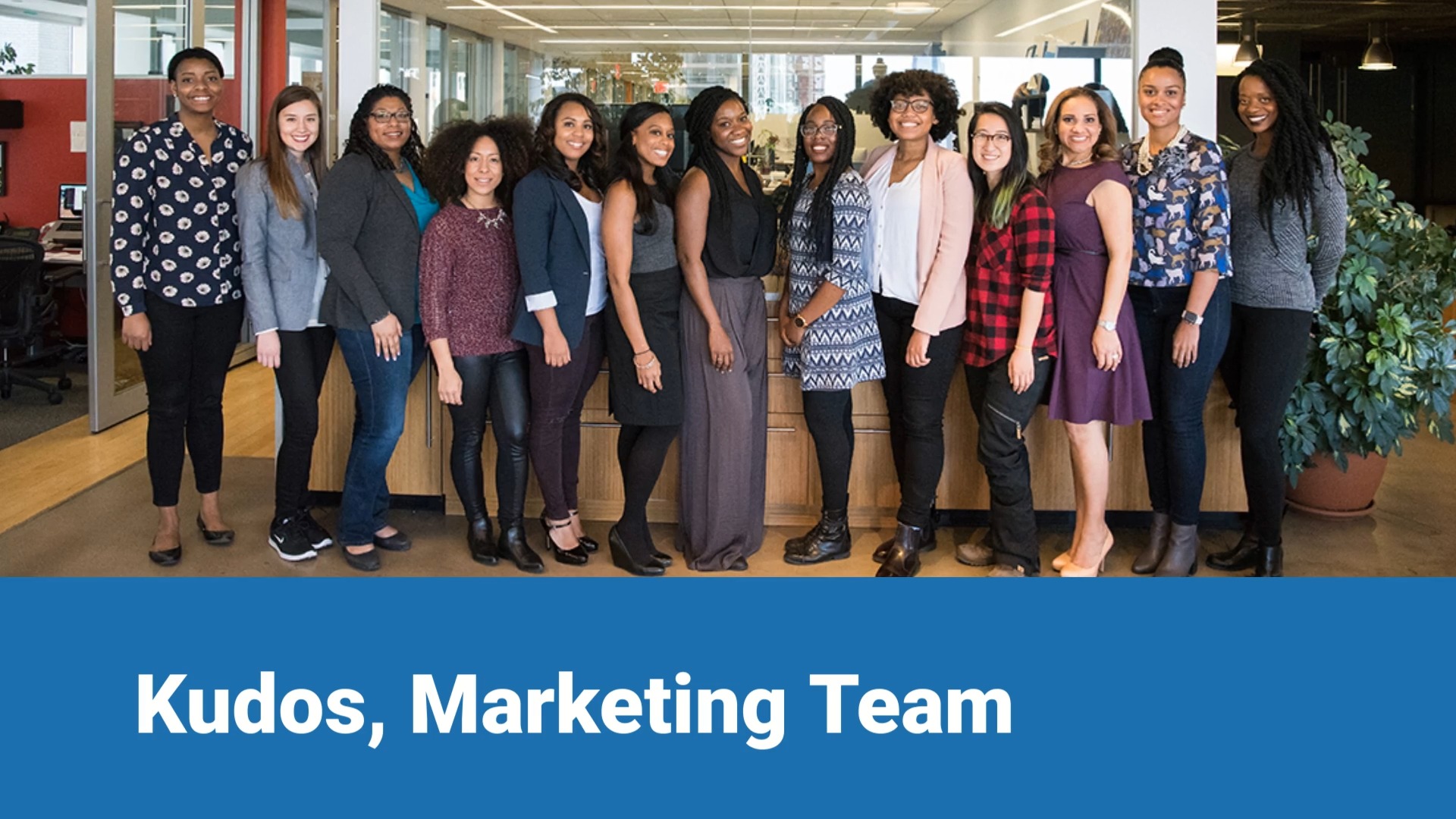 Group of eleven diverse women smiling and standing in a modern office environment, with a caption "kudos, marketing team" below them, featuring a Biteable video maker.