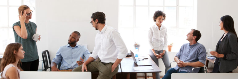 Two connected images of office workers in discussion; some are seated and talking, while others stand and gesture, in a bright, window-lit room designed for a Biteable video maker project.