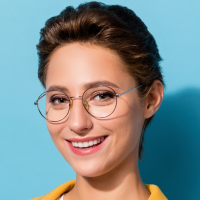 A joyful woman with short hair wearing round glasses smiles against a blue background.