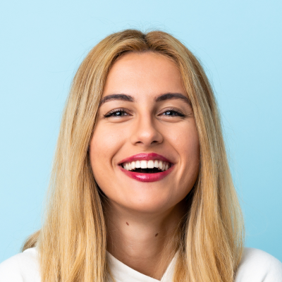 A young woman with blond hair smiling broadly against a light blue background.