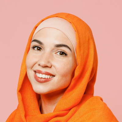 A woman with a bright orange hijab smiling, against a pink background.