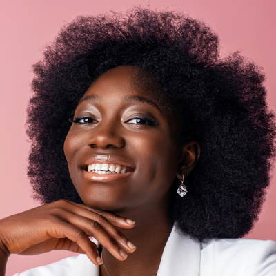 Portrait of a smiling Black woman with curly hair, wearing a white blouse and an earring, hand under chin, pink background.