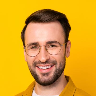 Man with a beard and glasses, smiling, wearing a yellow jacket against a yellow background.