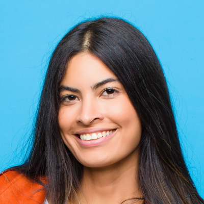 Portrait of a smiling woman with long dark hair wearing an orange top against a blue background.