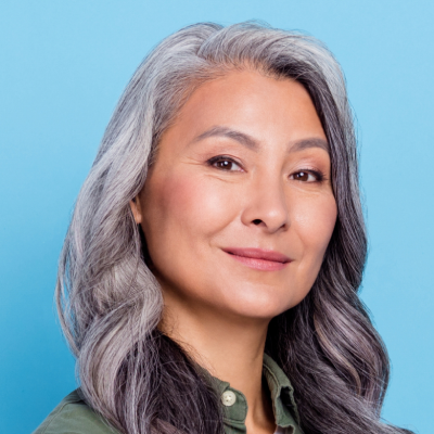 Middle-aged Asian woman with long gray hair smiling against a blue background.