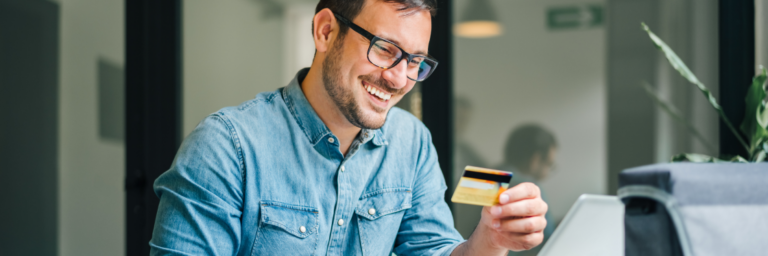 Man smiling while looking at a credit card and using a laptop.