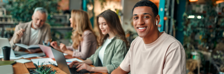 A diverse group of professionals working and interacting at a desk in a modern office, designed to motivate Gen Z, with lush greenery in the background.